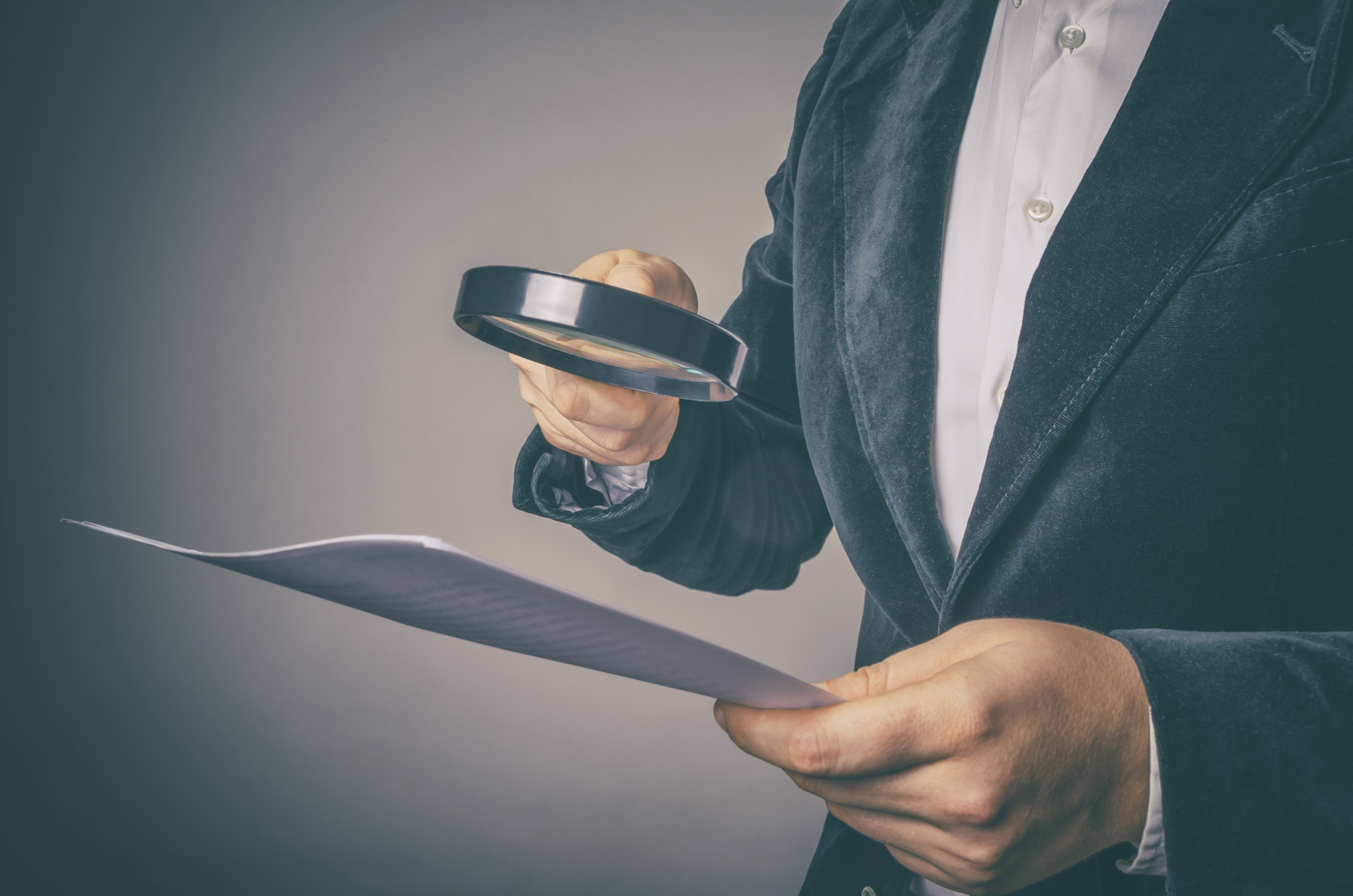 Image of a person holding a document in their hand with a magnifying glass
