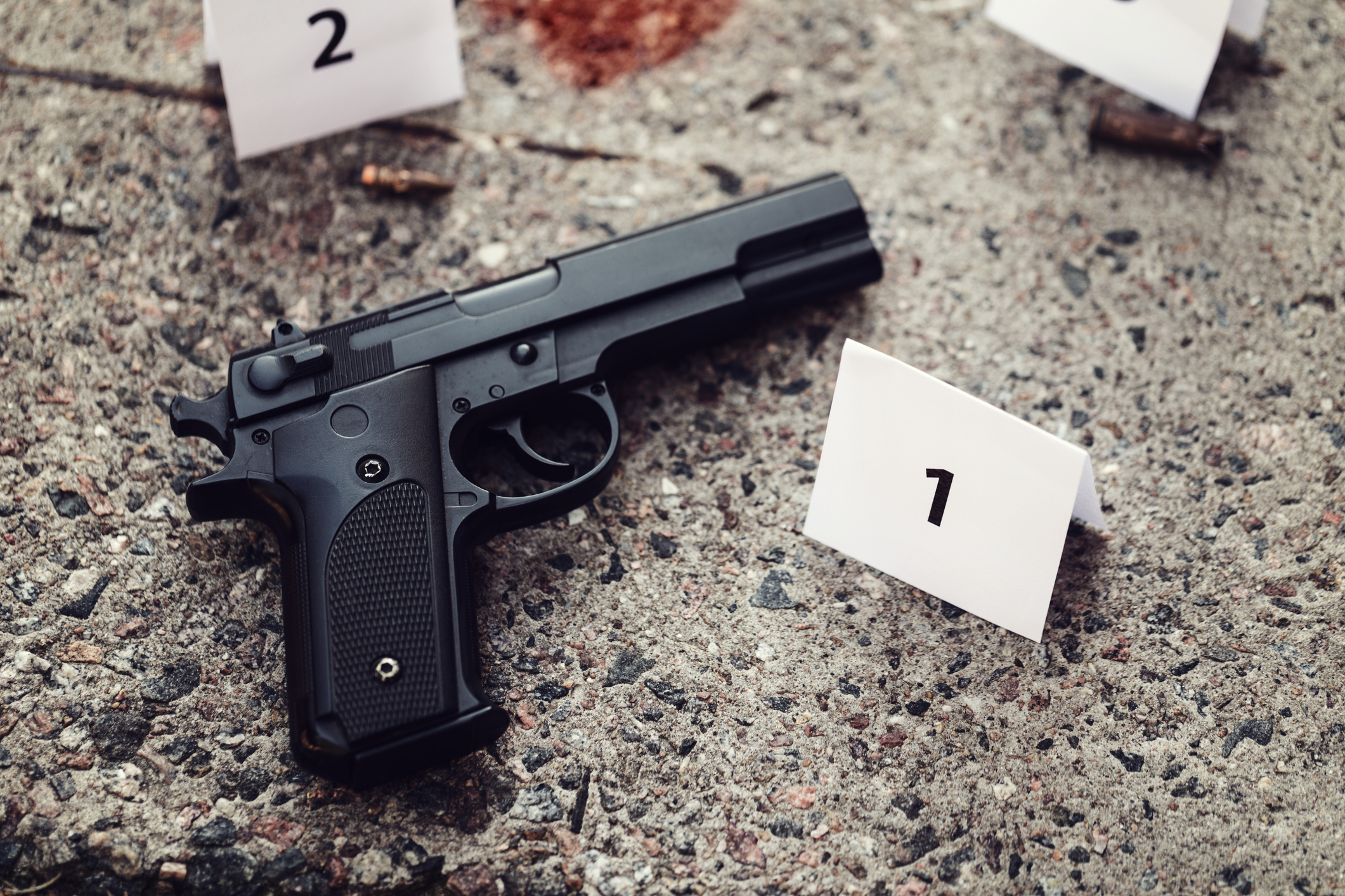 Handgun lying on bloodstained floor next to evidence markers. Handgun lying on bloodstained floor next to evidence markers.
