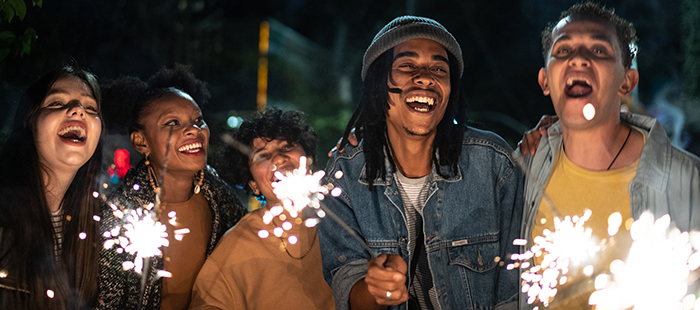 Diverse group of people holding fireworks and smiling at the camera.