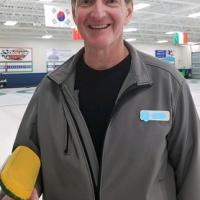 Ed holding a curling broom, standing on an ice rink.